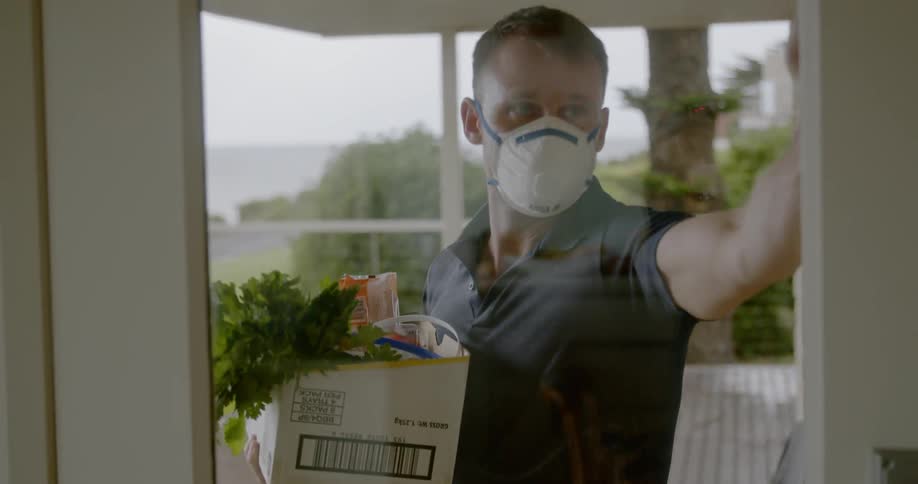 A man wearing a mask delivers groceries to a home
