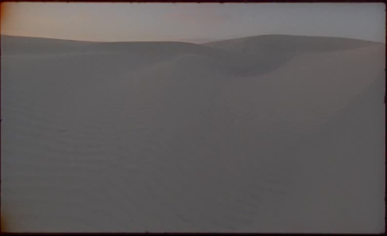 The sun sets over sand dunes in a desert
