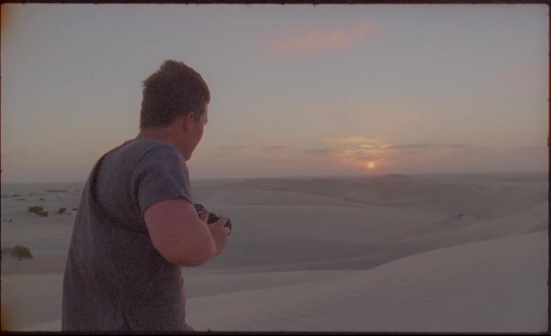 Man pulls up camera and takes photograph of sun setting over desert