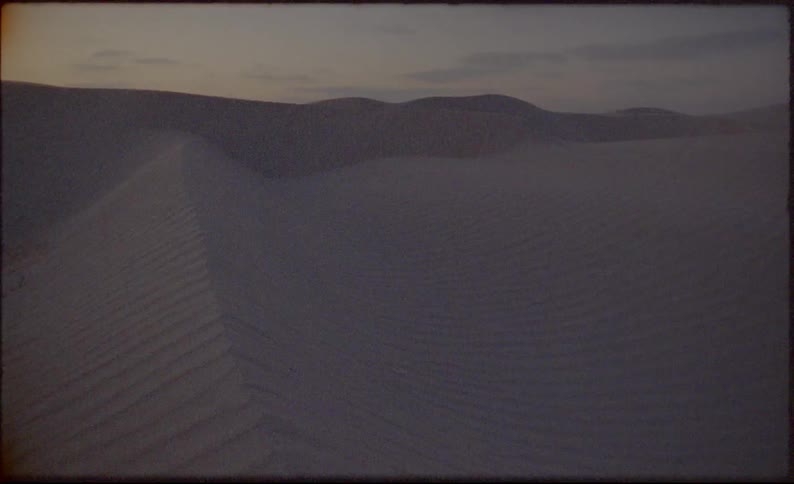 The sun sets over sand dunes in a desert