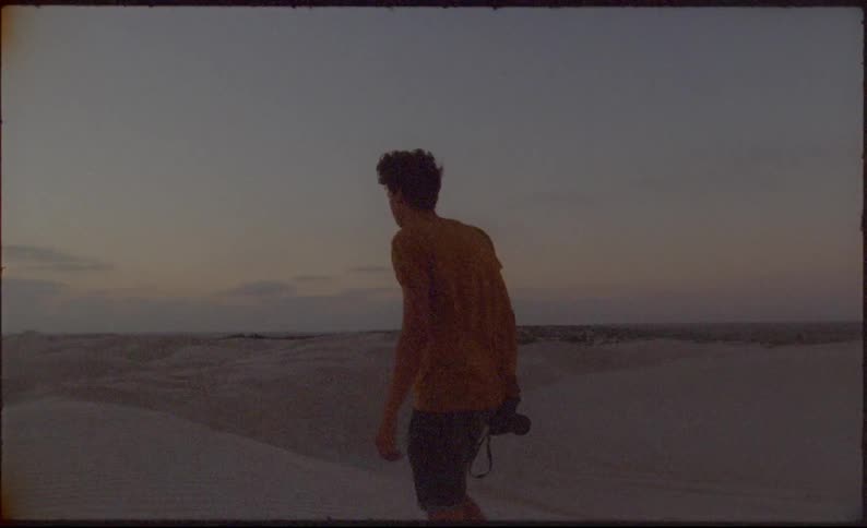 Man takes a photograph then walks along the beach as he carries the camera