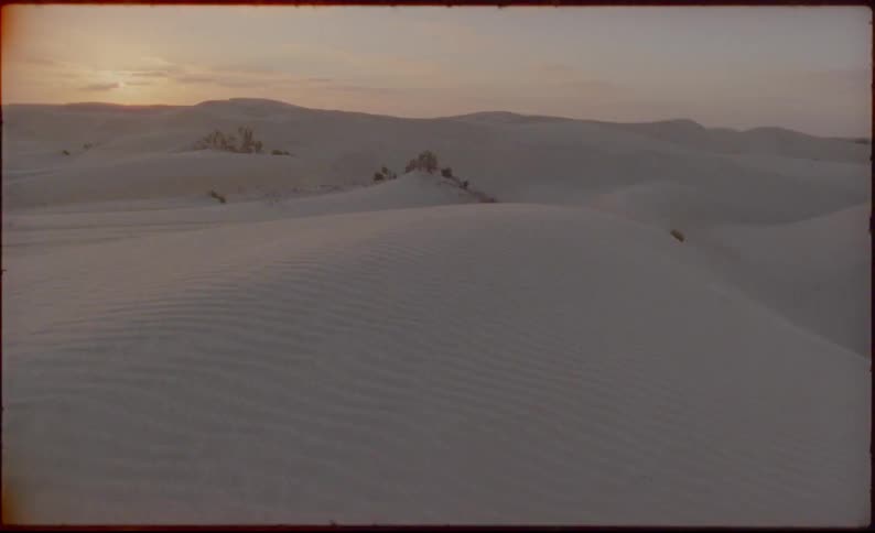Red colors the horizon near white sandy desert