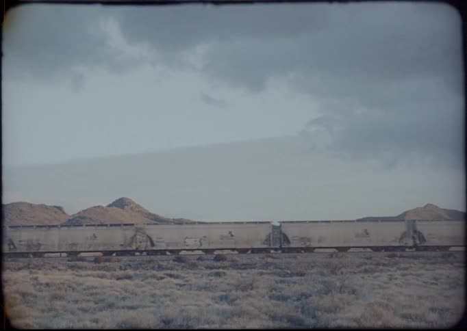 Vintage film of train moving on tracks in desert in front of mountains