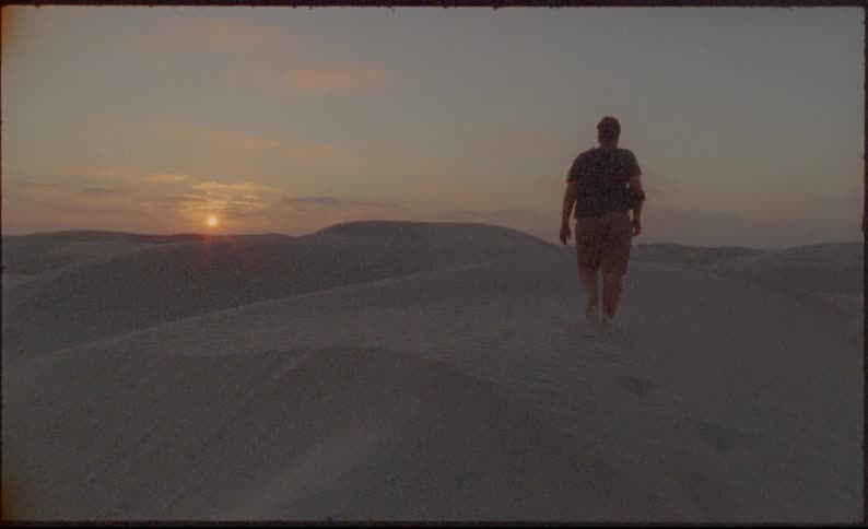 Man walking barefoot on a sand dune in a desert at sunset
