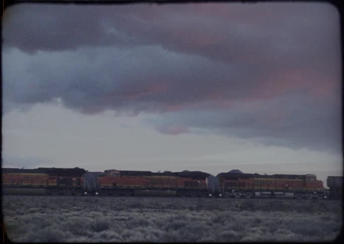 A train travels past brush and rocky hills on a cloudy day