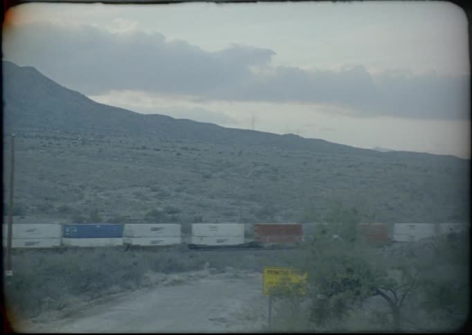 Train travels down the track near a field under a cloudy sky