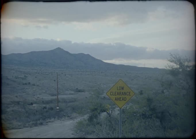 A dirt road with a low clearance ahead sign in front of mountains