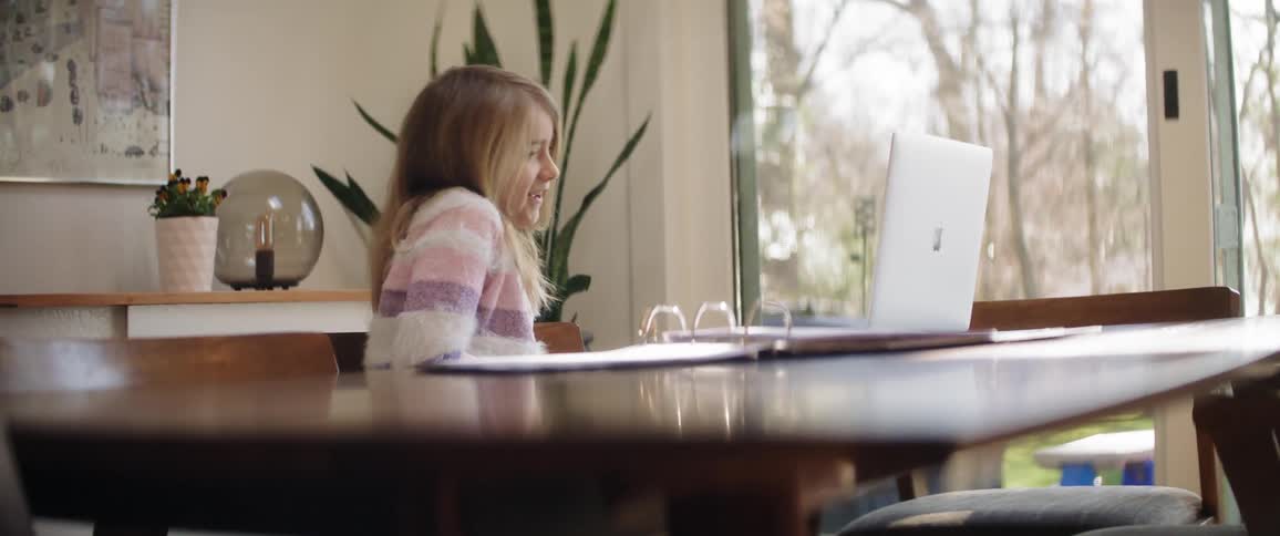 Girl grins as she sits at table and watches laptop