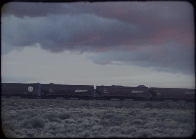 A long freight train with many cars travels through a desert landscape on a cloudy day