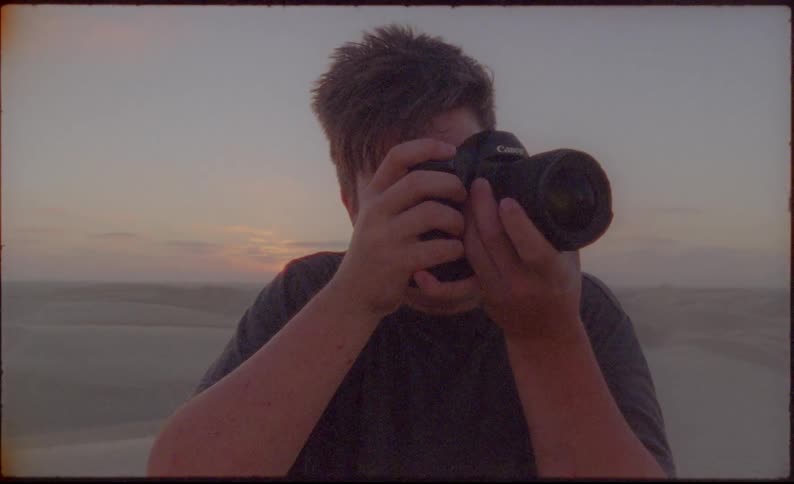 Photographer takes pictures of desert standing on sand dune at sunset