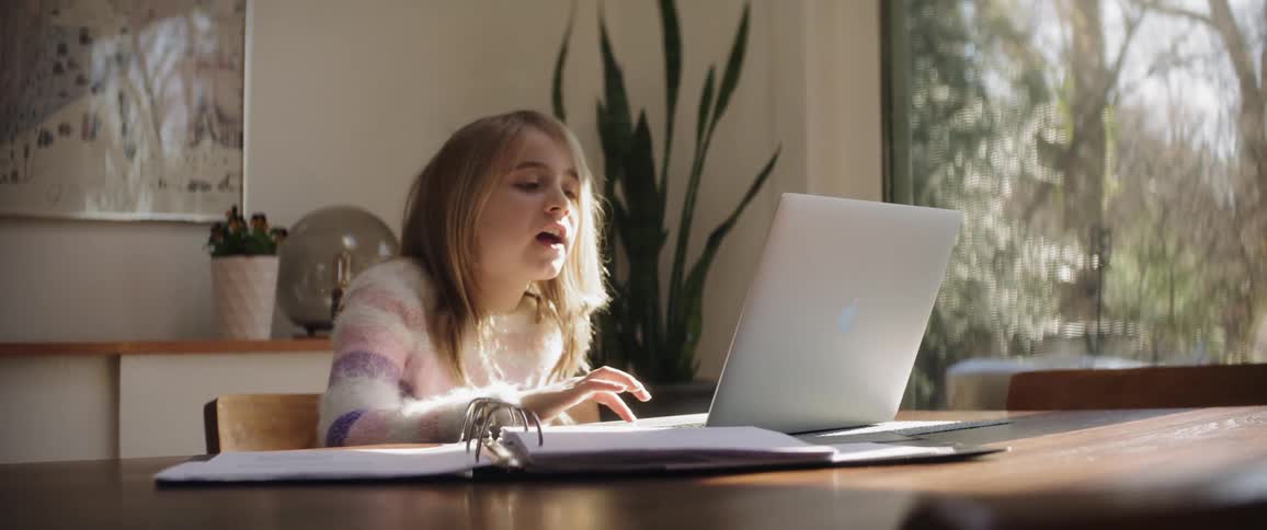 Girl smiles and talks while interacting with laptop at dining table