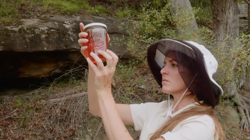 Woman holds up a jar of a red substance and examines it