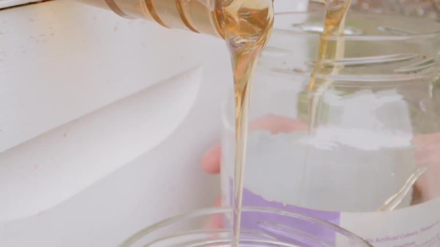 A person swaps jars under a spigot flowing with honey
