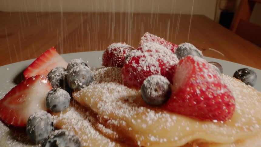 Powdered sugar is sprinkled onto pancakes with strawberries and blueberries