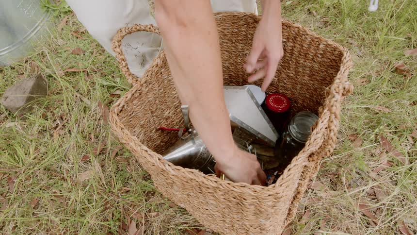 Woman places jar of honey into woven basket in grass