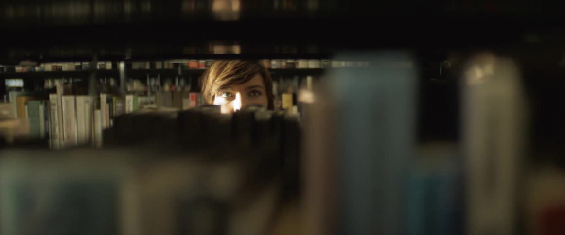 A woman walks in between library book shelves looking at the books