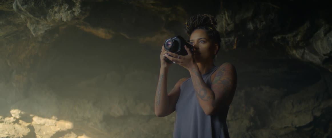 A woman with tattoos takes a photograph in a cave