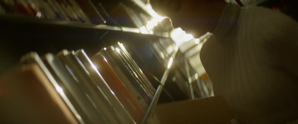 A woman takes a book off a library shelf and flips it open