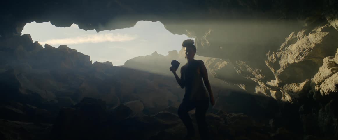 Young black woman walks into rocky cave holding video camera