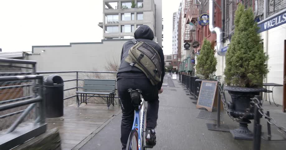 A person in a dark hoodie rides their bike in an alleyway