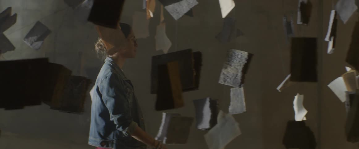 A woman walks through a room of art hanging from the ceiling