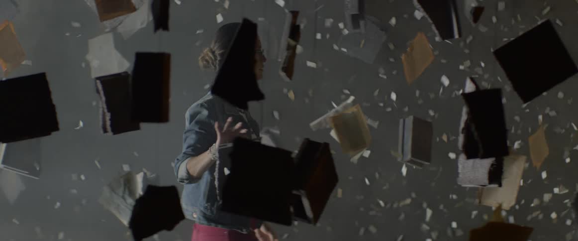 A woman walks past floating books and falling paper