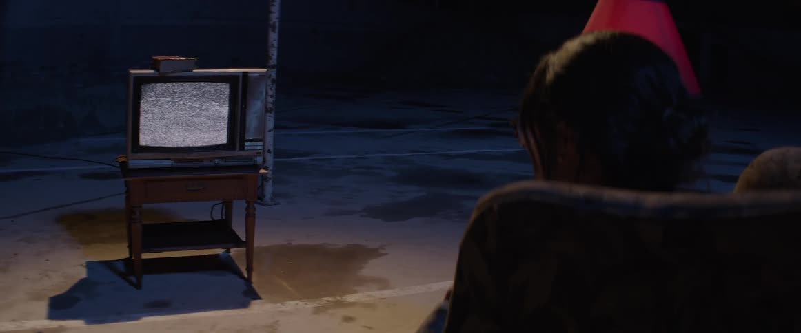 A woman sits in a chair and watches white noise on the old tv
