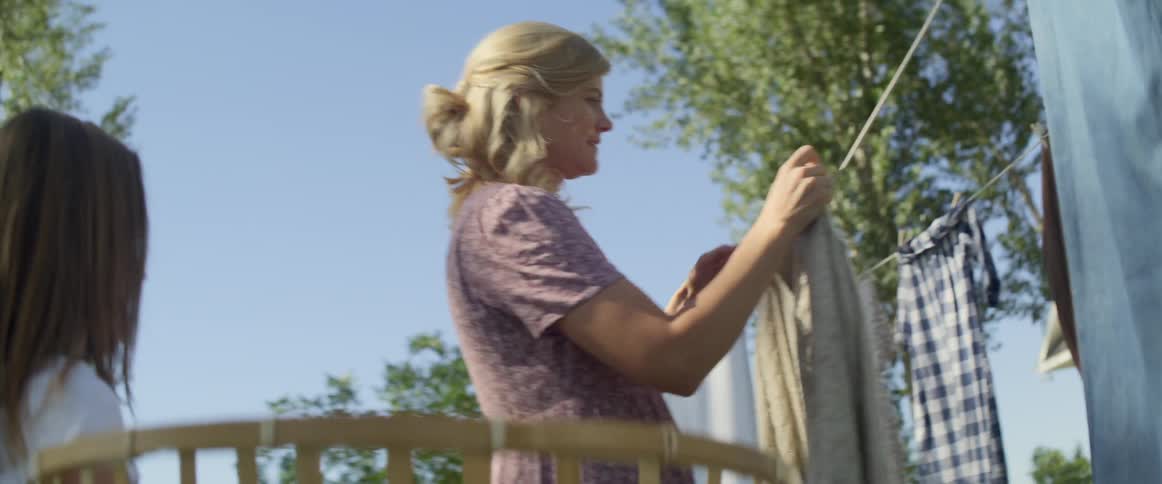 A woman shows her daughter how to hang clothing on a clothes line outdoors