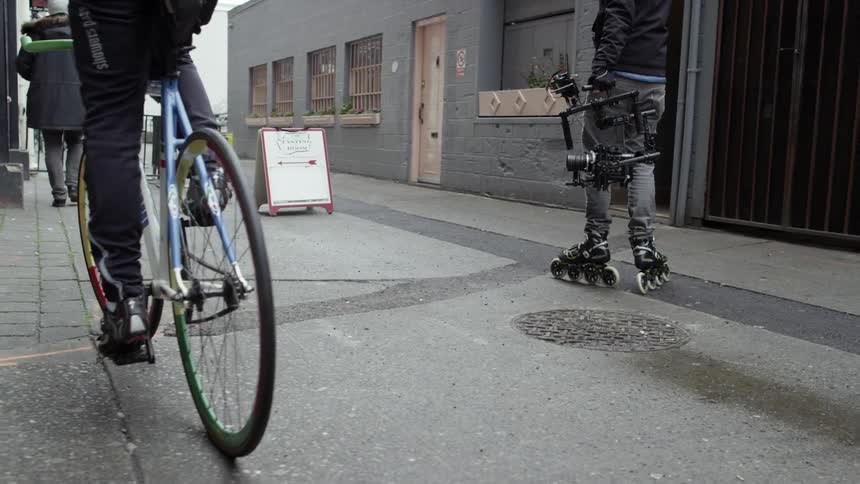 A man bikes in a city as a man in rollerblades stays at his side