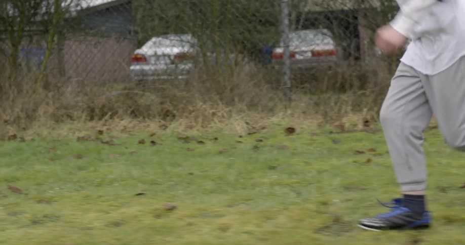 A boy in blue runs across grass next to a fence