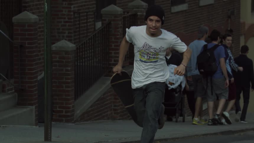 A man is running from a group of people holding a skateboard