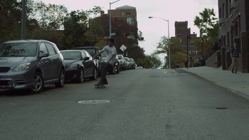 A young man riding a skateboard down a steep street in an urban area