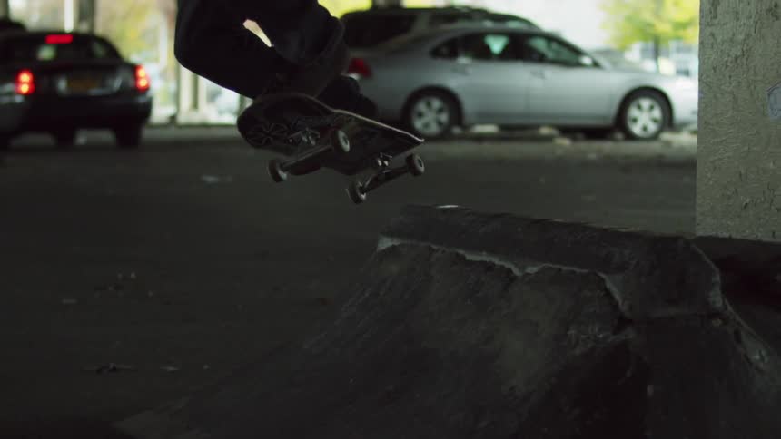 A teenager does a skateboard trick in an urban car park