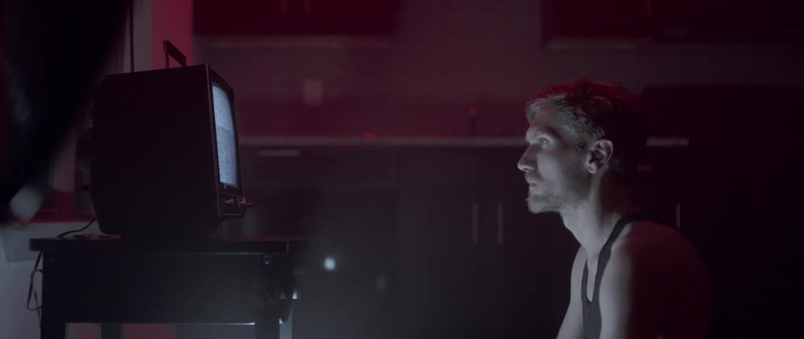 A man sitting before a television displaying static in a dark room