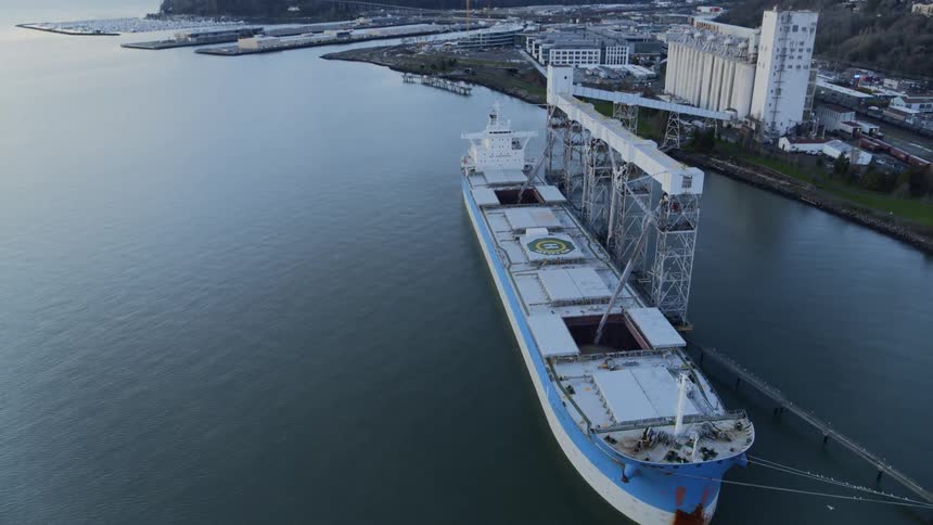Grain pours into the cargo hold of an enormous ship docked at a port terminal
