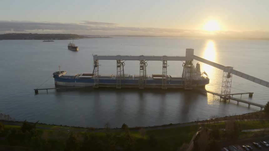A bulk cargo vessel is loaded at port while another waits its turn offshore