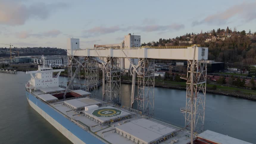 Pullback reveal of a docked cargo vessel being loaded from a grain shipping terminal