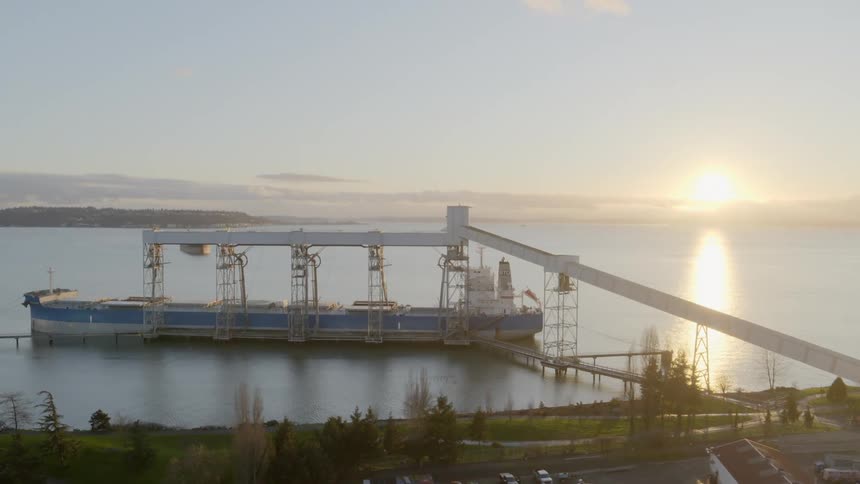 A large cargo ship is loaded with grain as the sun sets in the distance