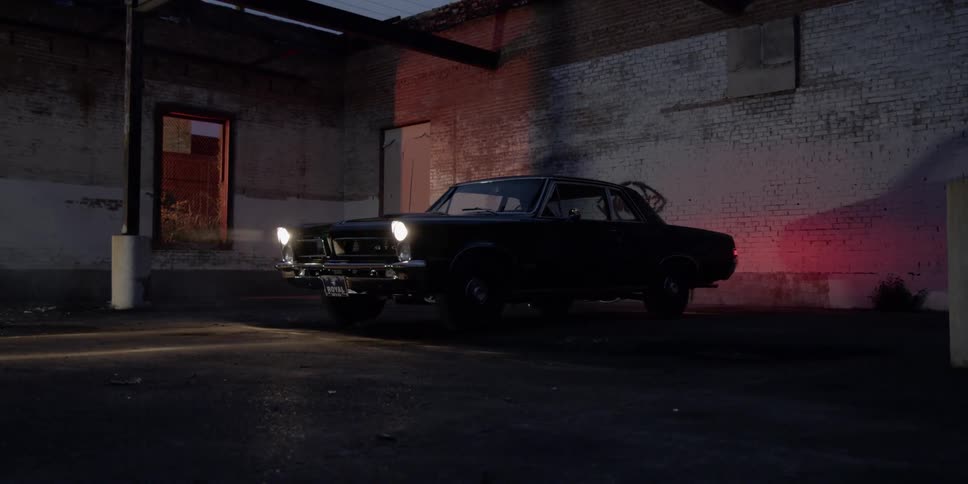 A car with headlights on in an empty parking area next to a building at night