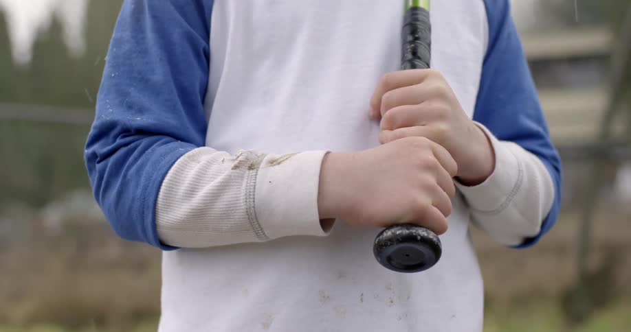 Boy standing outside holding a bat in the sprinkling rain