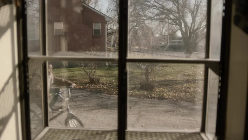 A window looking out onto a road where a boy is riding a bicycle