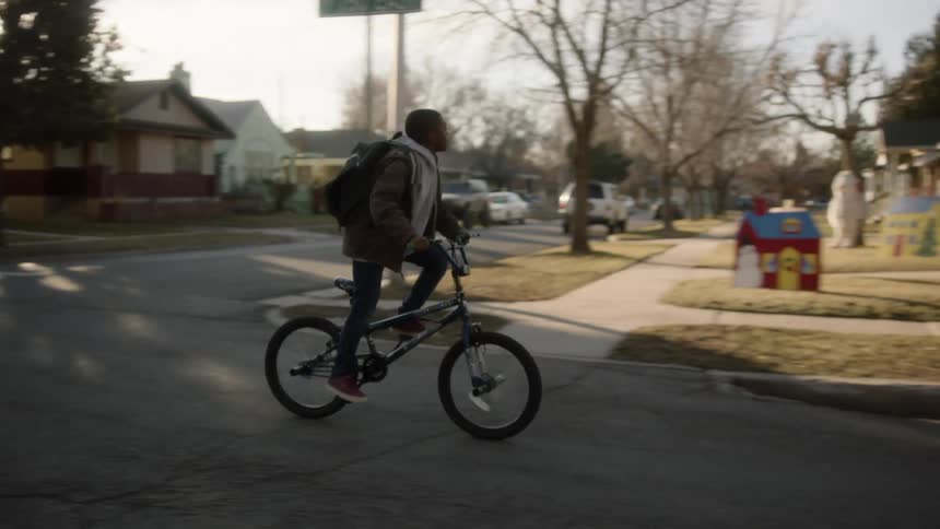 A teenager rides his bike through the intersection of a neighborhood