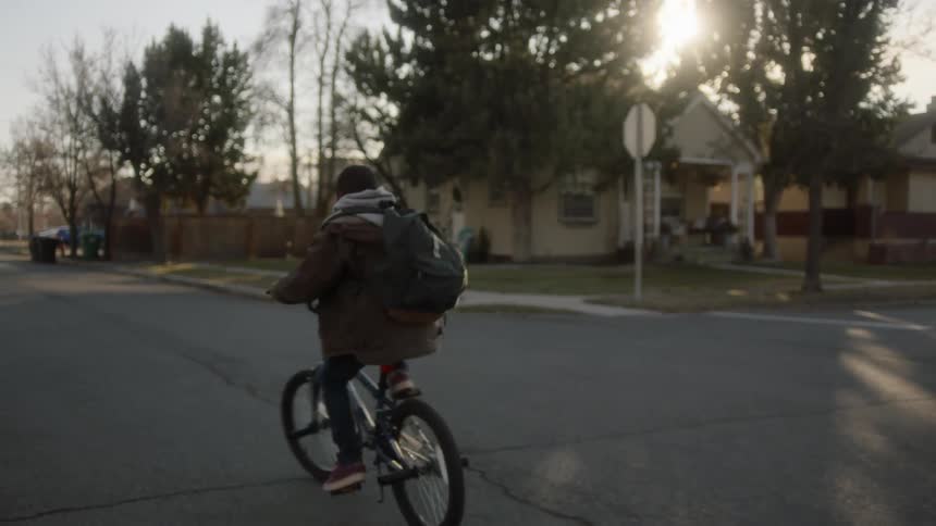 Boy bicycles along street in residential neighborhood