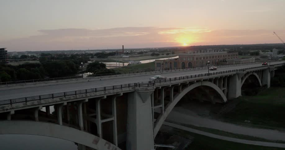 Cars driving out of city on bridge over river at sunset