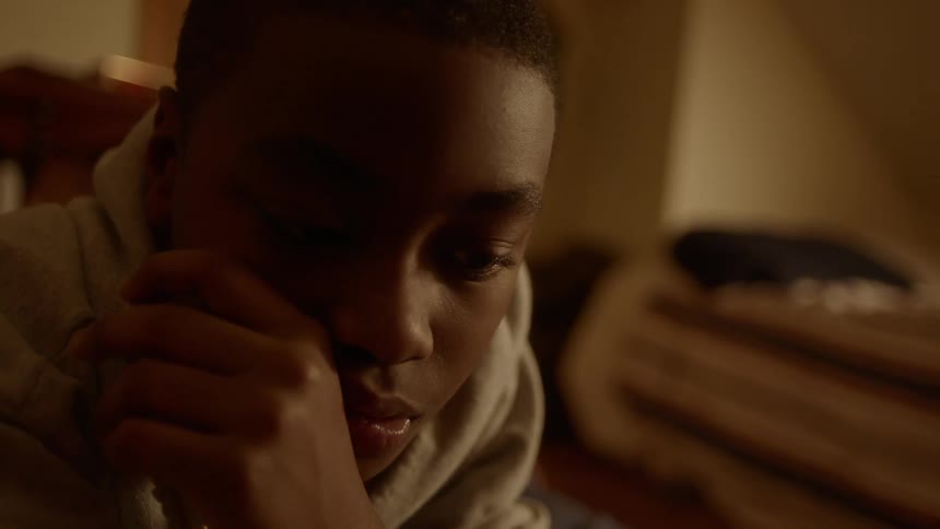 A boy touches his face while laying on his stomach on the floor of his bedroom