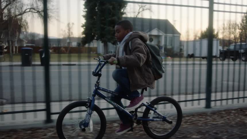 A boy is riding his bike past the fence