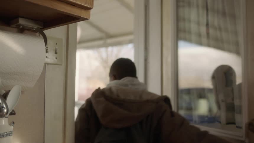 Young boy wearing a jacket and backpack opens the back door in the kitchen walks out and closes the door behind him