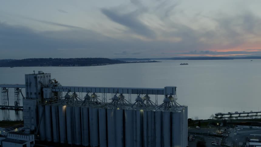 Revealing the tall silos of an international grain shipping terminal along the waterfront at sunset