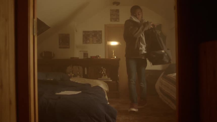 A boy picks up his backpack and walks out of his bedroom