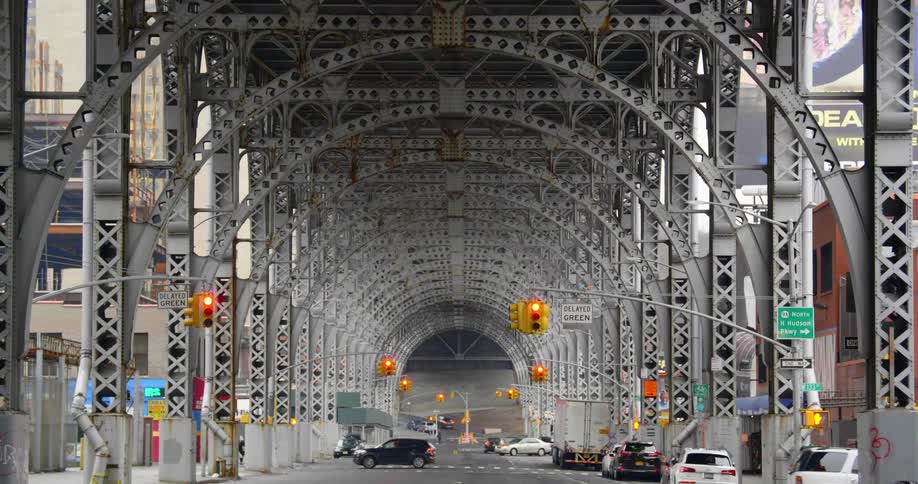 Cars pass under arched supports under bridge in city